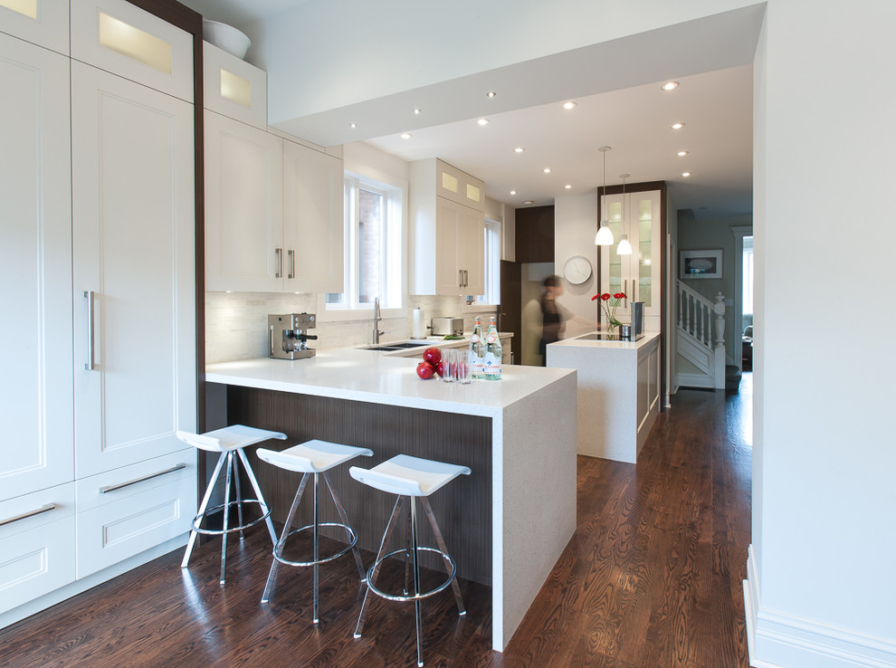 Photo of a contemporary galley open plan kitchen in Toronto with recessed-panel cabinets, a double-bowl sink, white cabinets, limestone benchtops, white splashback, stainless steel appliances, medium hardwood floors, multiple islands and limestone splashback.