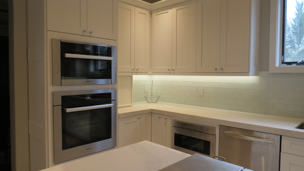 Example of a large transitional l-shaped light wood floor and beige floor enclosed kitchen design with a double-bowl sink, shaker cabinets, white cabinets, marble countertops, blue backsplash, glass tile backsplash, stainless steel appliances and an island