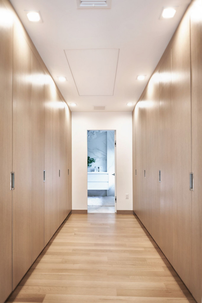 This is an example of a mid-sized contemporary gender-neutral storage and wardrobe in New York with flat-panel cabinets, light wood cabinets, light hardwood floors and beige floor.