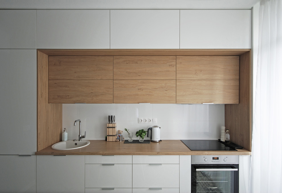 This is an example of a mid-sized contemporary single-wall open plan kitchen in Other with a drop-in sink, flat-panel cabinets, white cabinets, laminate benchtops, white splashback, porcelain splashback, stainless steel appliances, porcelain floors and no island.