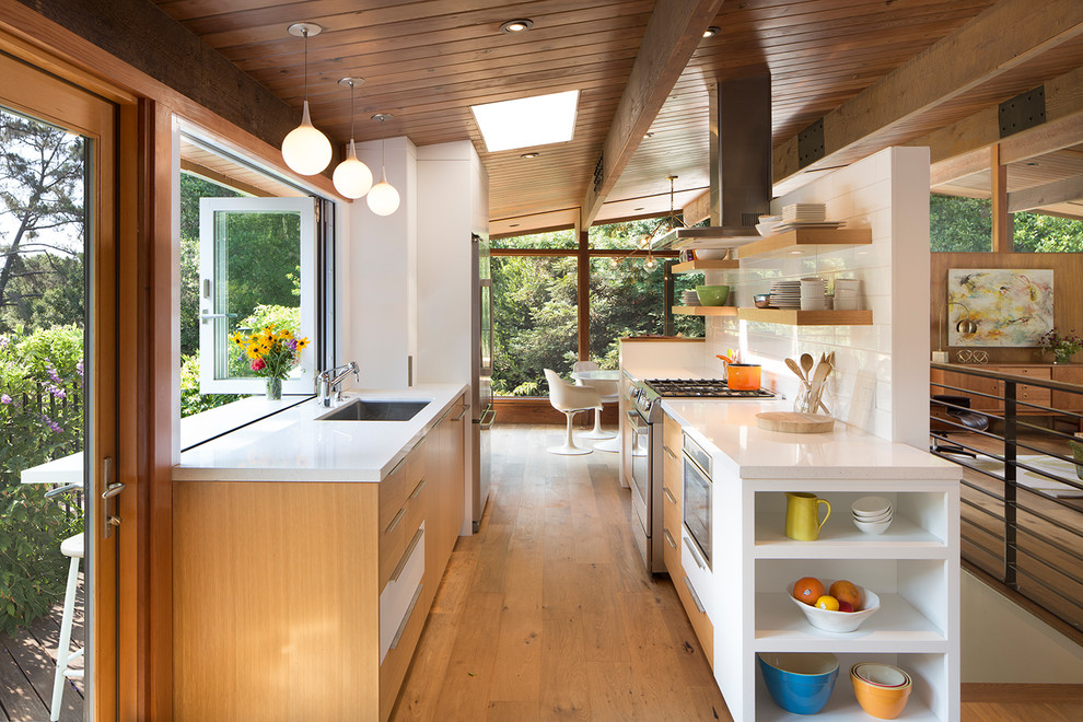 Inspiration for a midcentury galley kitchen in San Francisco with an undermount sink, flat-panel cabinets, medium wood cabinets, white splashback, subway tile splashback, stainless steel appliances, medium hardwood floors, a peninsula, brown floor and white benchtop.