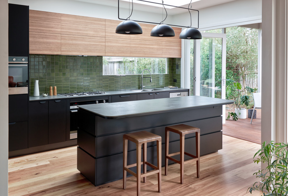 Photo of a mid-sized contemporary l-shaped eat-in kitchen in Melbourne with flat-panel cabinets, black cabinets, laminate benchtops, green splashback, porcelain splashback, stainless steel appliances, light hardwood floors, with island and grey benchtop.