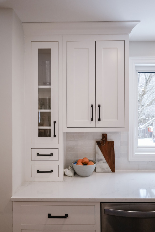 Example of a small transitional u-shaped medium tone wood floor and brown floor eat-in kitchen design in Ottawa with an undermount sink, shaker cabinets, white cabinets, quartz countertops, white backsplash, subway tile backsplash, stainless steel appliances, an island and white countertops