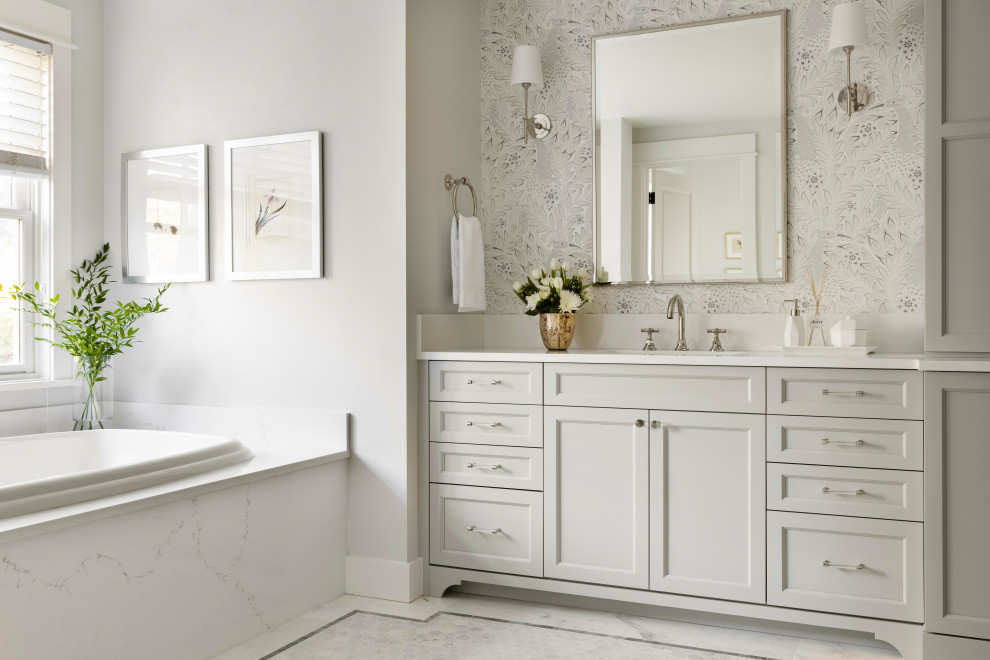 Large transitional master white tile and marble tile marble floor, white floor, double-sink and wallpaper bathroom photo with recessed-panel cabinets, gray cabinets, a two-piece toilet, gray walls, an undermount sink, quartz countertops, a hinged shower door, white countertops and a built-in vanity