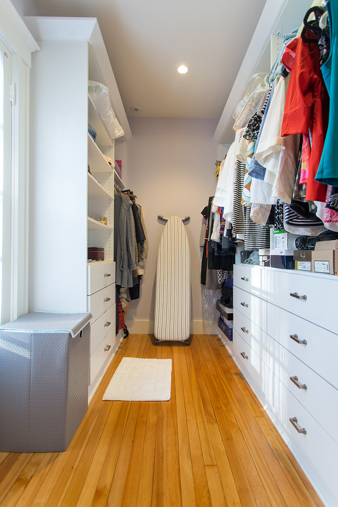 Photo of a mid-sized country gender-neutral walk-in wardrobe in Boston with flat-panel cabinets, white cabinets and light hardwood floors.