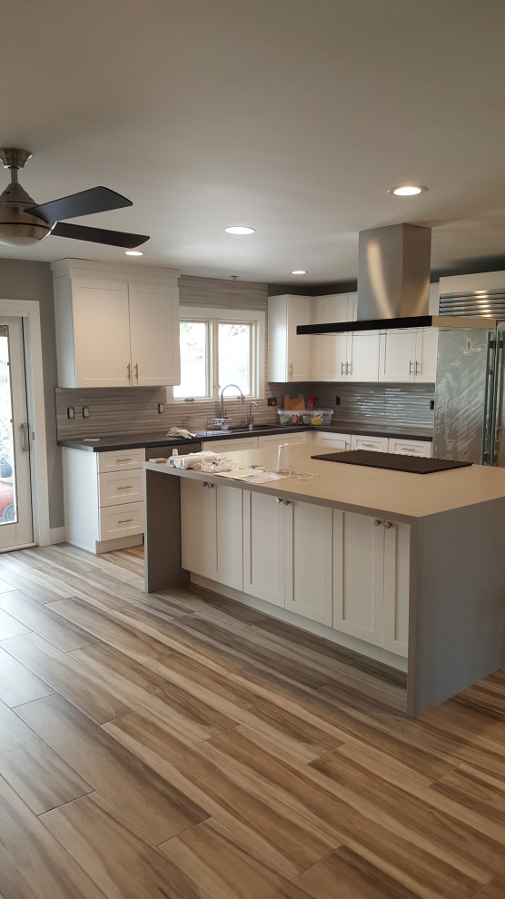 This is an example of a large modern u-shaped kitchen in Los Angeles with a built-in sink, shaker cabinets, white cabinets, composite countertops, grey splashback, ceramic splashback, stainless steel appliances, light hardwood flooring, brown floors and grey worktops.