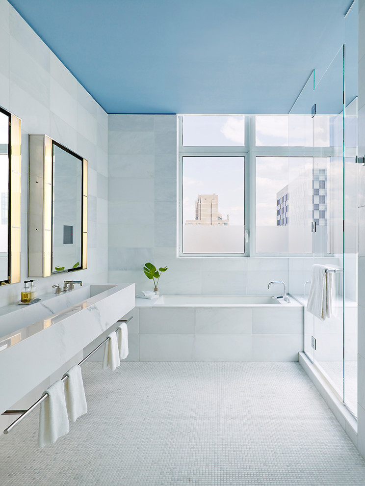Photo of a contemporary bathroom in New York with an undermount tub, an alcove shower, white tile, mosaic tile floors, a trough sink, white floor, a hinged shower door and white benchtops.