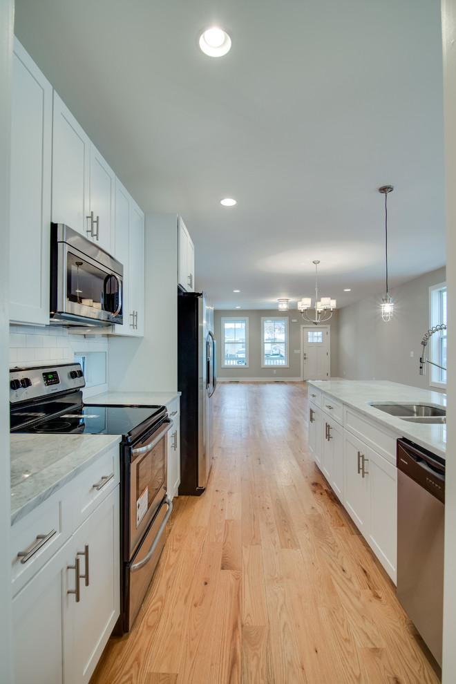This is an example of a mid-sized traditional galley eat-in kitchen in Nashville with a double-bowl sink, white cabinets, granite benchtops, white splashback, stainless steel appliances, light hardwood floors and with island.