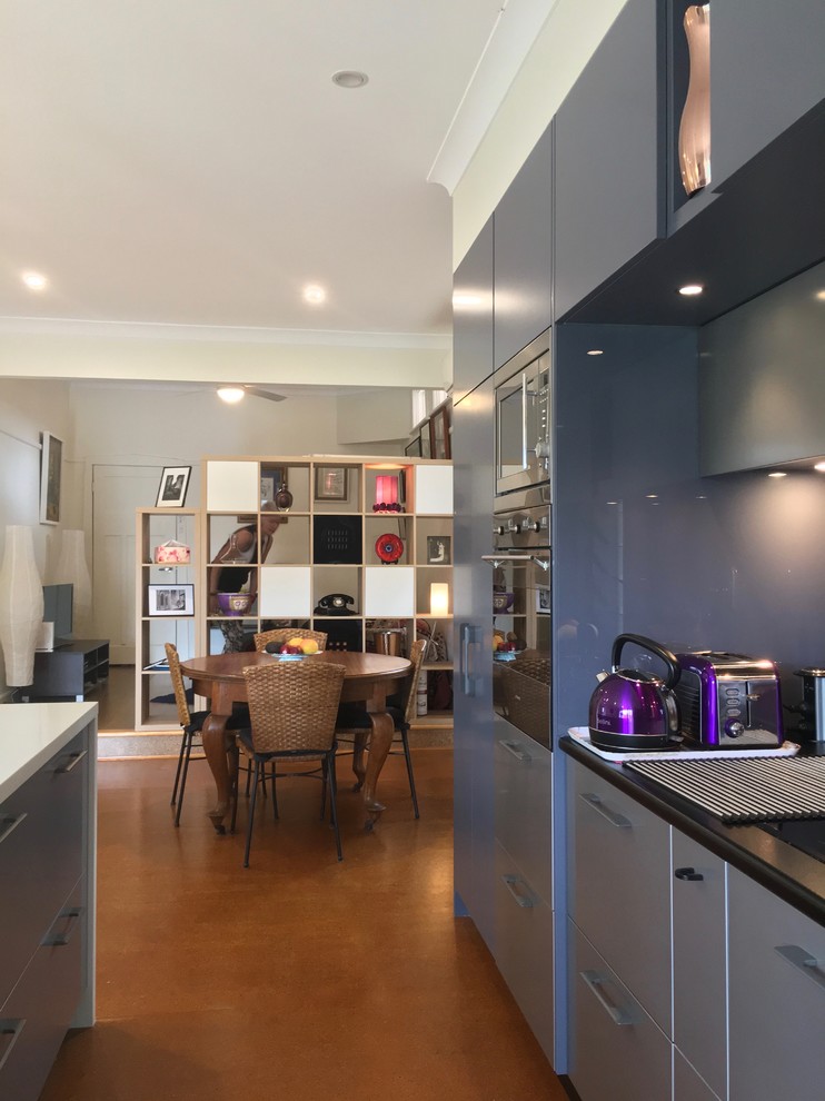 Photo of a small modern galley open plan kitchen in Sydney with an undermount sink, flat-panel cabinets, blue cabinets, quartzite benchtops, metallic splashback, glass sheet splashback, stainless steel appliances, painted wood floors, with island, orange floor and white benchtop.