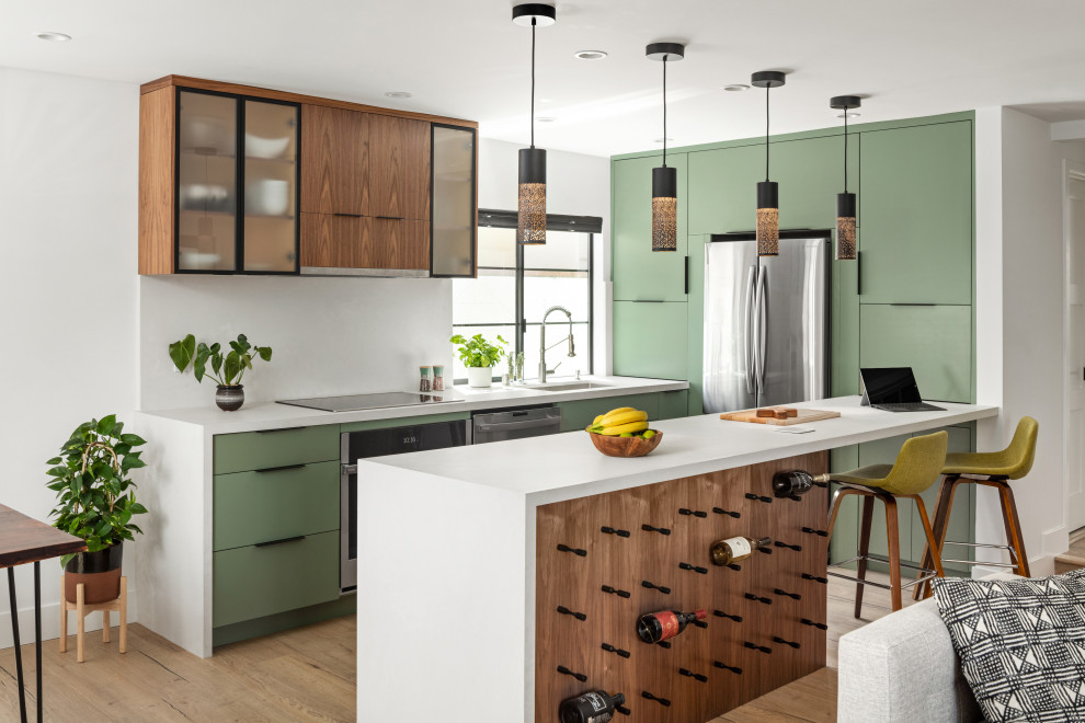Inspiration for a small contemporary galley open plan kitchen in Los Angeles with an undermount sink, flat-panel cabinets, green cabinets, quartz benchtops, white splashback, engineered quartz splashback, stainless steel appliances, light hardwood floors, a peninsula, brown floor and white benchtop.