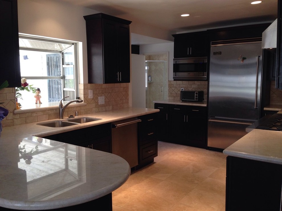 Example of a mid-sized transitional u-shaped limestone floor and beige floor enclosed kitchen design with a double-bowl sink, shaker cabinets, black cabinets, granite countertops, beige backsplash, brick backsplash, stainless steel appliances, a peninsula and beige countertops