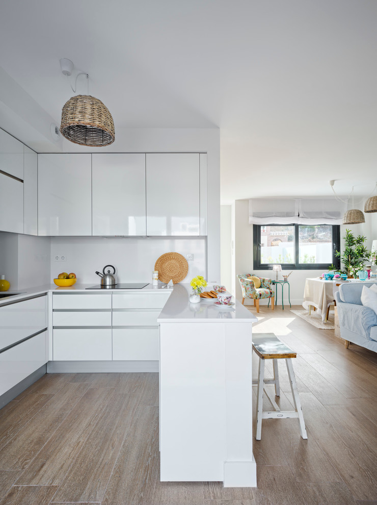 This is an example of a mid-sized beach style open plan kitchen in Malaga with flat-panel cabinets, white cabinets and white splashback.