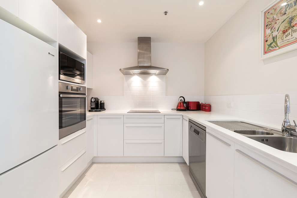 Inspiration for a mid-sized contemporary u-shaped open plan kitchen in Auckland with a double-bowl sink, flat-panel cabinets, white cabinets, quartz benchtops, white splashback, subway tile splashback, porcelain floors and beige floor.