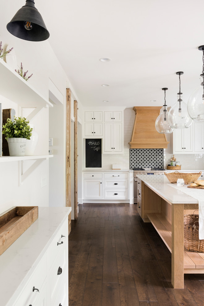 This is an example of a large modern kitchen pantry in Minneapolis with a farmhouse sink, beaded inset cabinets, white cabinets, quartzite benchtops, white splashback, stainless steel appliances, dark hardwood floors, with island, brown floor and white benchtop.