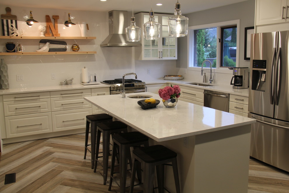 Inspiration for a large transitional l-shaped vinyl floor and brown floor open concept kitchen remodel in Vancouver with an undermount sink, recessed-panel cabinets, white cabinets, quartz countertops, white backsplash, ceramic backsplash, stainless steel appliances and an island
