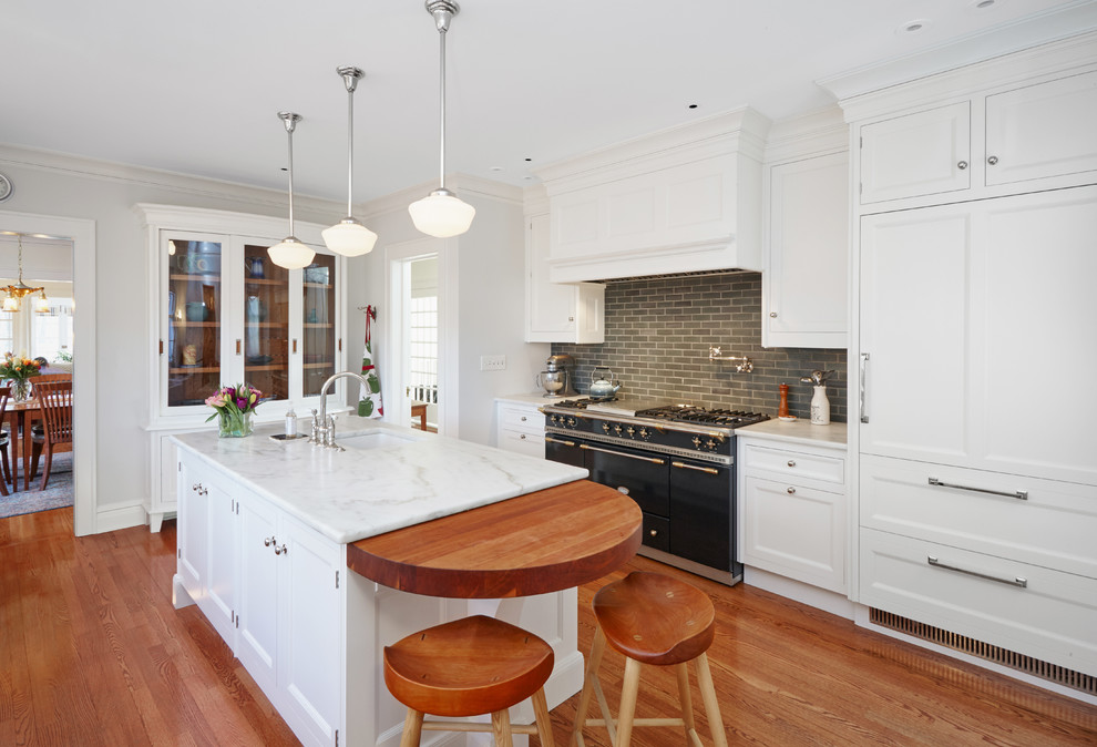This is an example of a traditional l-shaped separate kitchen in Chicago with an undermount sink, shaker cabinets, white cabinets, grey splashback, subway tile splashback, black appliances, medium hardwood floors, with island and white benchtop.