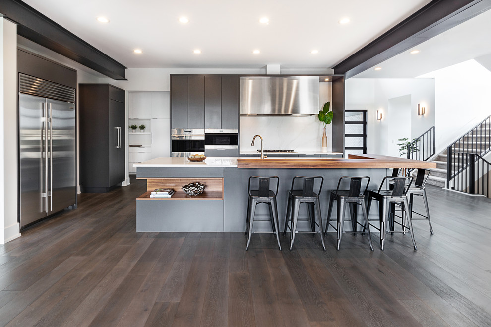 Example of a trendy dark wood floor kitchen design in Edmonton with flat-panel cabinets, gray cabinets, white backsplash, stainless steel appliances, an island and white countertops