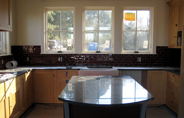 Example of a transitional kitchen design in Boston with a farmhouse sink, light wood cabinets, black backsplash, white appliances and an island
