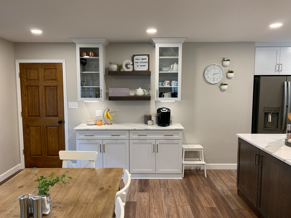 Example of a large transitional u-shaped vinyl floor and brown floor open concept kitchen design with an undermount sink, shaker cabinets, white cabinets, quartz countertops, white backsplash, ceramic backsplash, stainless steel appliances, an island and white countertops