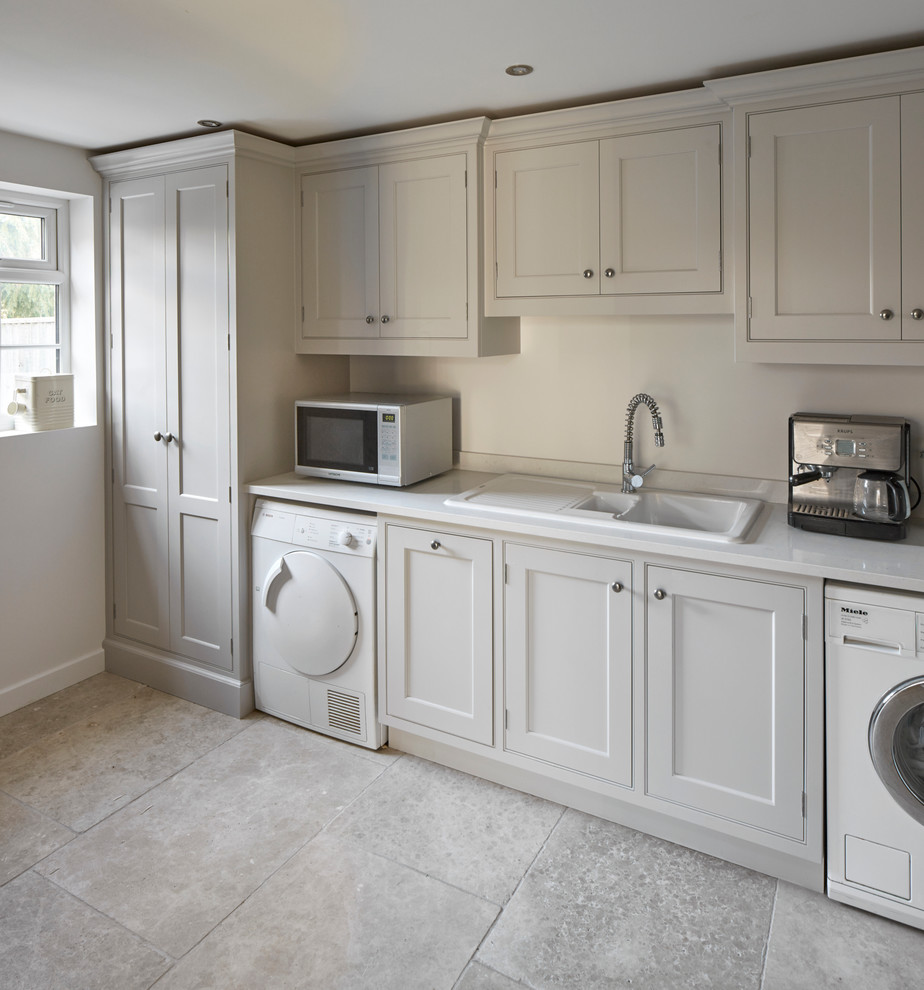 Large traditional single-wall utility room in Wiltshire with grey cabinets, quartz benchtops, beige splashback, stone slab splashback, limestone floors, a drop-in sink, beaded inset cabinets and white walls.