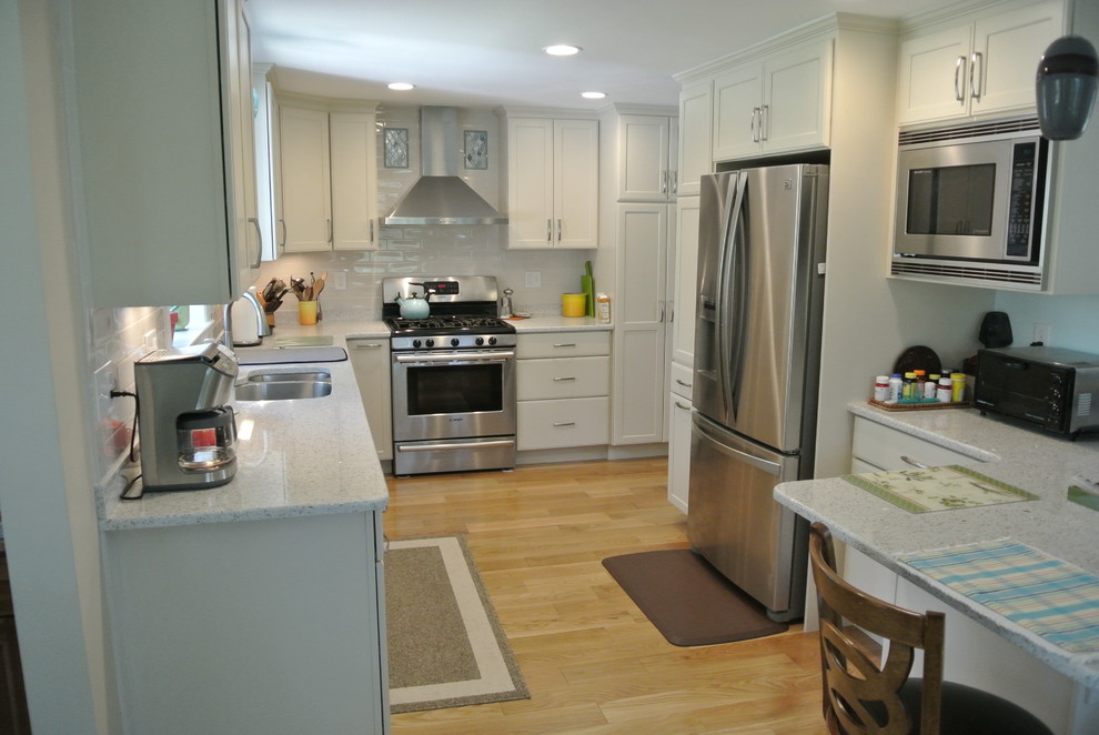 Transitional l-shaped medium tone wood floor eat-in kitchen photo in Boston with an undermount sink, shaker cabinets, white cabinets, recycled glass countertops, white backsplash, subway tile backsplash, stainless steel appliances, a peninsula and white countertops