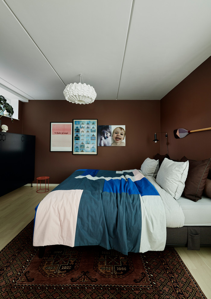Large contemporary master bedroom in Copenhagen with brown walls, light hardwood floors, no fireplace and beige floor.