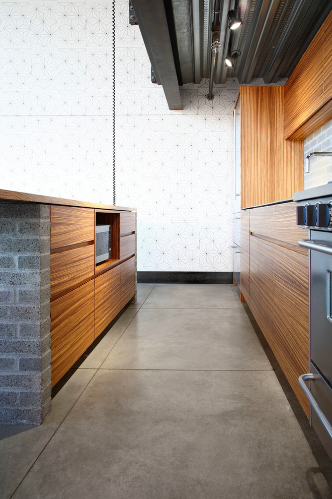 Inspiration for a mid-sized modern kitchen in Seattle with an undermount sink, flat-panel cabinets, medium wood cabinets, wood benchtops, grey splashback, brick splashback, stainless steel appliances, concrete floors, with island and grey floor.