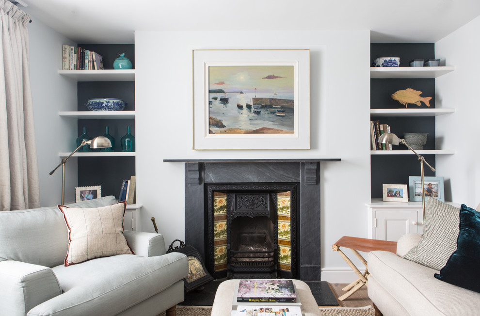 This is an example of a beach style living room in London with a library, white walls and a standard fireplace.
