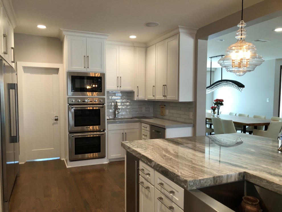 Open concept kitchen - large transitional l-shaped medium tone wood floor and brown floor open concept kitchen idea in Dallas with an undermount sink, shaker cabinets, white cabinets, quartz countertops, gray backsplash, ceramic backsplash, stainless steel appliances and an island