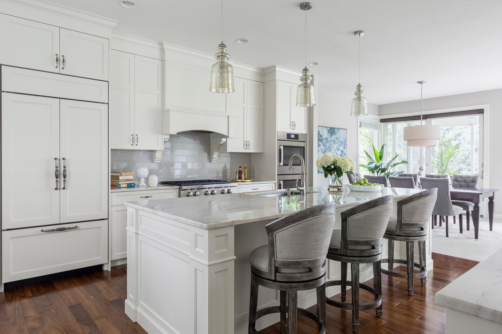 Photo of a traditional galley eat-in kitchen in Minneapolis with an undermount sink, beaded inset cabinets, white cabinets, grey splashback, subway tile splashback, panelled appliances, medium hardwood floors, with island, brown floor and grey benchtop.