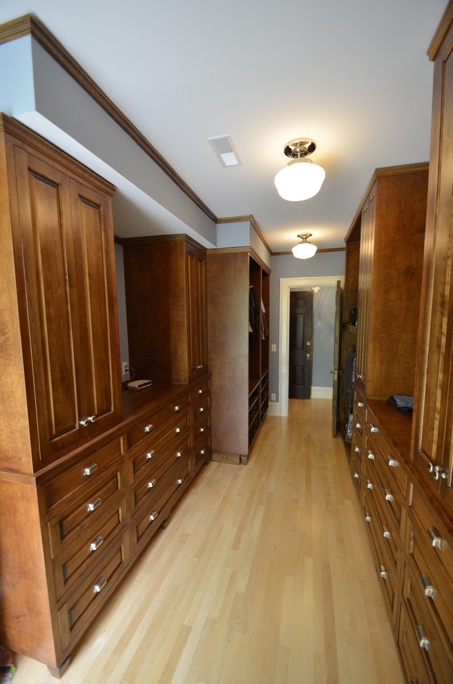This is an example of a large traditional gender-neutral dressing room in Milwaukee with distressed cabinets, light hardwood floors and recessed-panel cabinets.