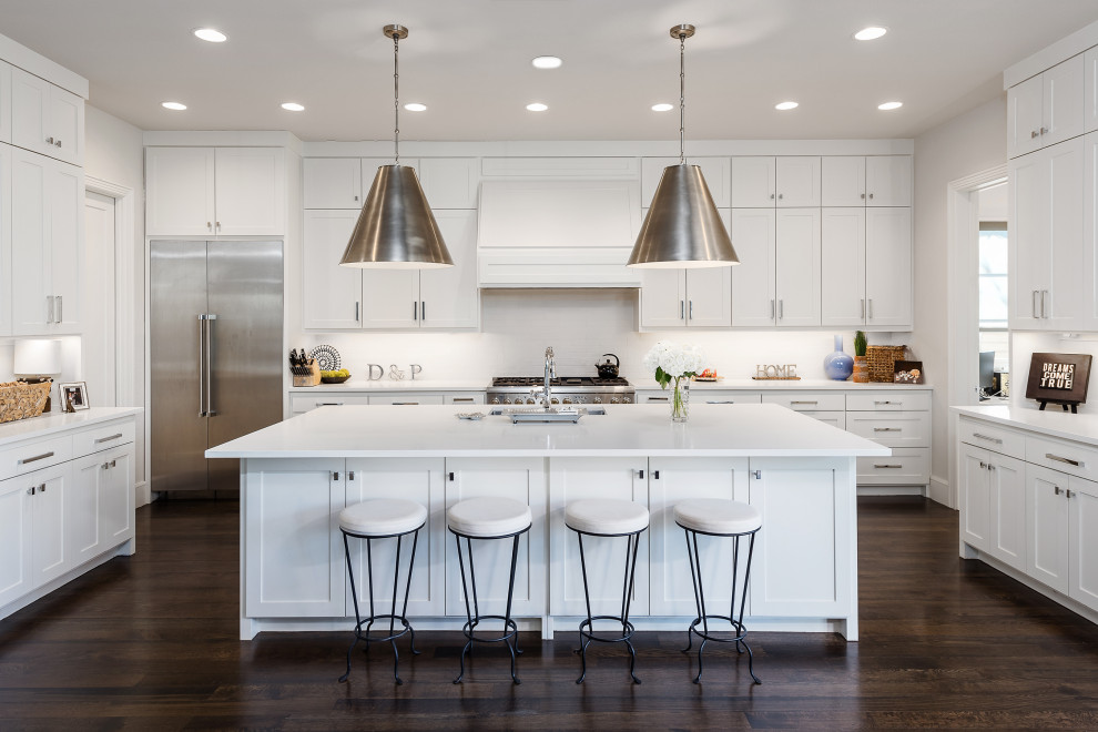 Inspiration for a transitional u-shaped dark wood floor and brown floor kitchen remodel with an undermount sink, shaker cabinets, white cabinets, white backsplash, stainless steel appliances, an island and white countertops