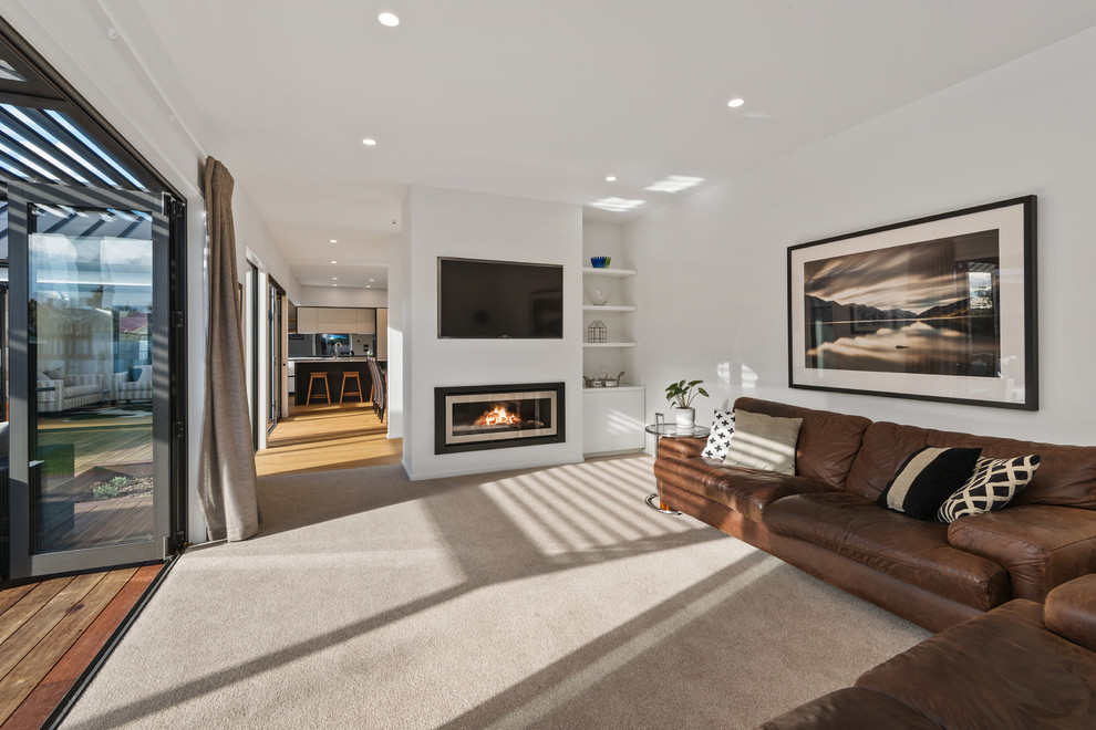 Photo of a mid-sized modern formal open concept living room in Christchurch with carpet, a standard fireplace, a plaster fireplace surround, a wall-mounted tv and beige floor.