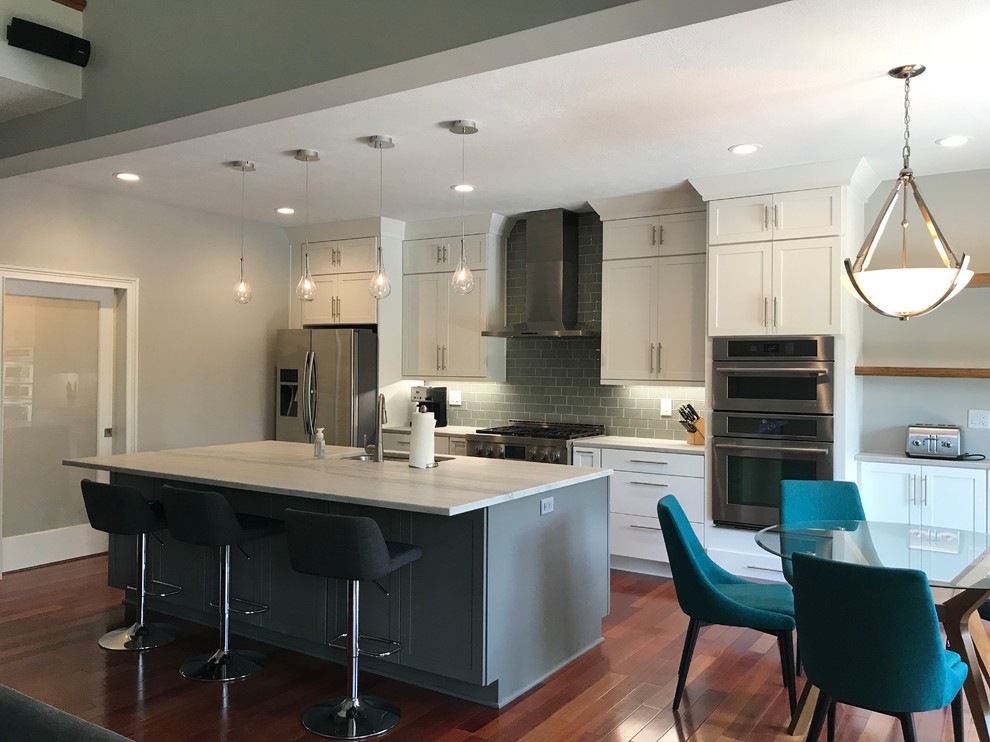 Example of a mid-sized transitional single-wall medium tone wood floor and brown floor eat-in kitchen design with an undermount sink, shaker cabinets, white cabinets, quartzite countertops, gray backsplash, glass tile backsplash, stainless steel appliances, an island and multicolored countertops