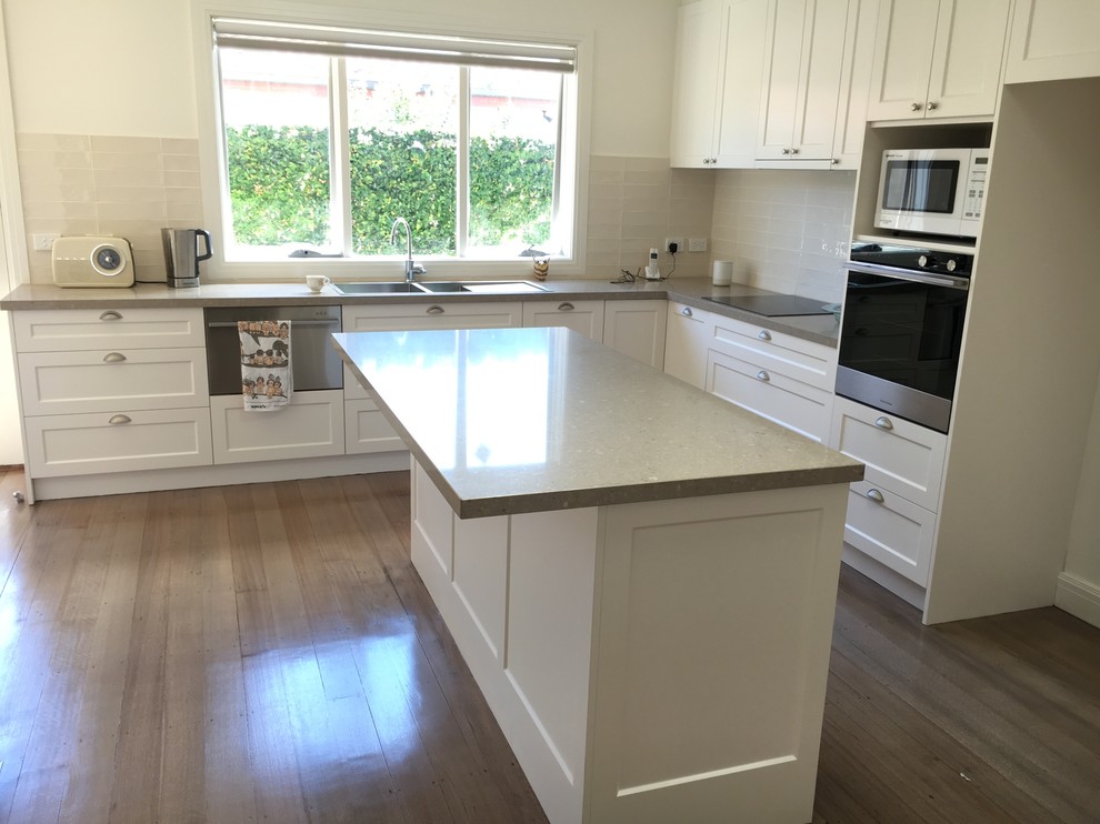 Photo of a large traditional l-shaped kitchen in Melbourne with a double-bowl sink, shaker cabinets, limestone benchtops, beige splashback, subway tile splashback, stainless steel appliances, dark hardwood floors and with island.