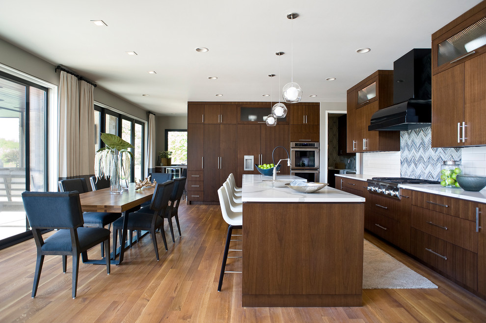 Large transitional l-shaped medium tone wood floor and brown floor eat-in kitchen photo with a farmhouse sink, flat-panel cabinets, dark wood cabinets, marble countertops, white backsplash, subway tile backsplash, paneled appliances and an island