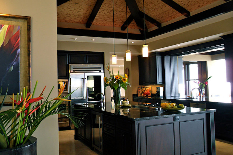 This is an example of a large tropical u-shaped eat-in kitchen in Hawaii with an undermount sink, raised-panel cabinets, dark wood cabinets, granite benchtops, green splashback, stone slab splashback, stainless steel appliances, travertine floors and multiple islands.