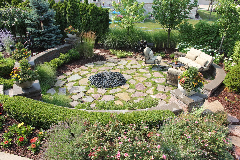 This is an example of a traditional full sun garden for summer in Chicago with a water feature and natural stone pavers.