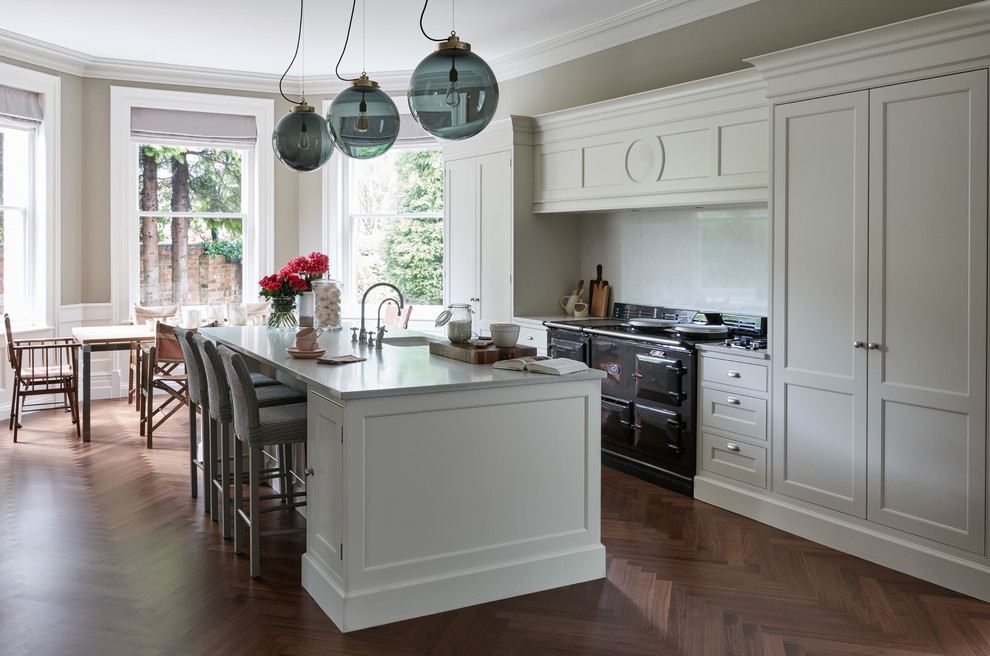 This is an example of a large traditional galley open plan kitchen in London with a drop-in sink, shaker cabinets, yellow cabinets, quartzite benchtops, black appliances, dark hardwood floors, multiple islands and yellow benchtop.