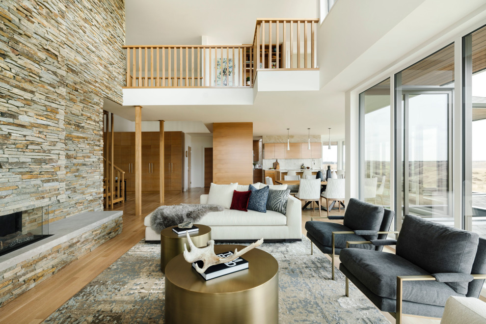 Inspiration for a large contemporary formal open plan living room in Calgary with white walls, light hardwood flooring, a two-sided fireplace, a stacked stone fireplace surround, no tv and beige floors.
