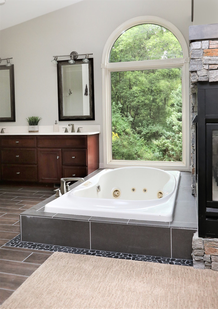 Drop-in bathtub - mid-sized transitional master gray tile and pebble tile pebble tile floor and gray floor drop-in bathtub idea with raised-panel cabinets, medium tone wood cabinets, gray walls and an integrated sink