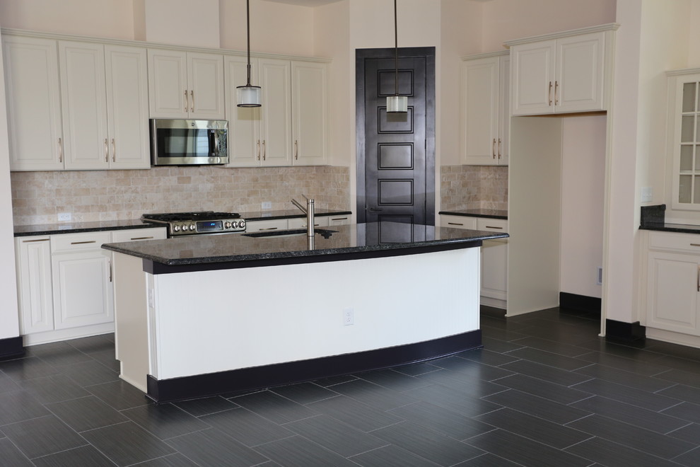 This is an example of a mid-sized traditional l-shaped eat-in kitchen in Jacksonville with an undermount sink, raised-panel cabinets, white cabinets, granite benchtops, beige splashback, travertine splashback, stainless steel appliances, porcelain floors, with island and black floor.
