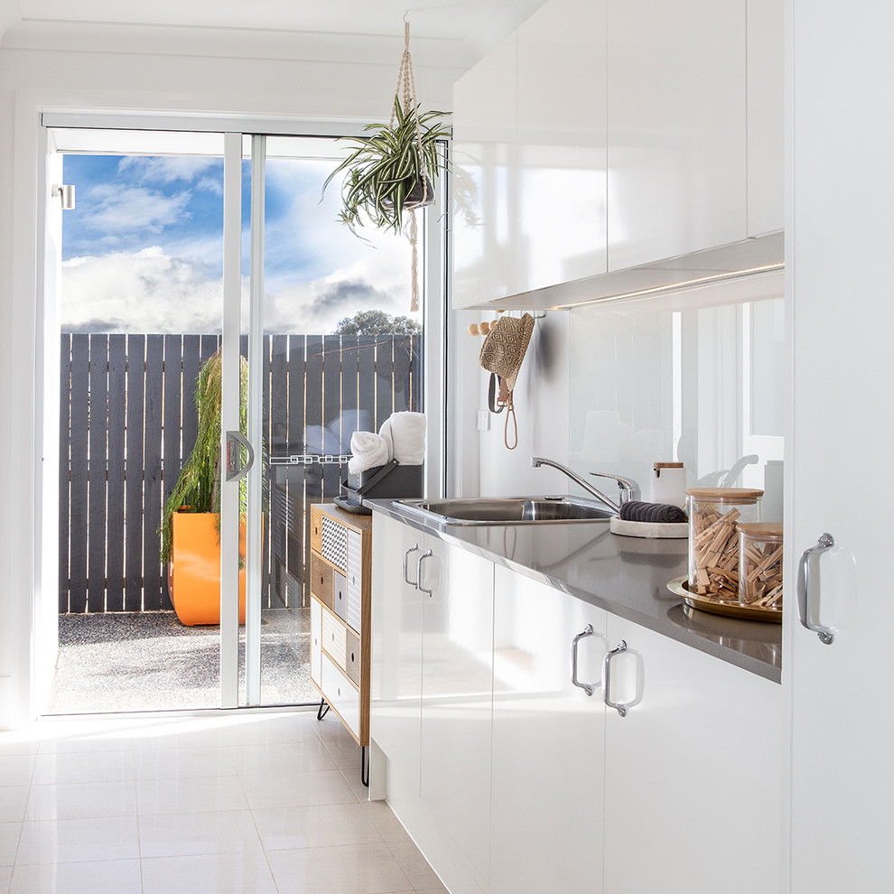 Midcentury galley dedicated laundry room in Canberra - Queanbeyan with a drop-in sink, white cabinets, granite benchtops, white walls, ceramic floors, grey benchtop, flat-panel cabinets and white floor.