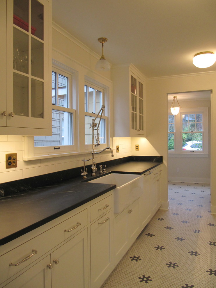 Inspiration for a small traditional galley separate kitchen in Seattle with a farmhouse sink, recessed-panel cabinets, white cabinets, marble benchtops, black splashback, marble splashback, panelled appliances, ceramic floors, no island and white floor.