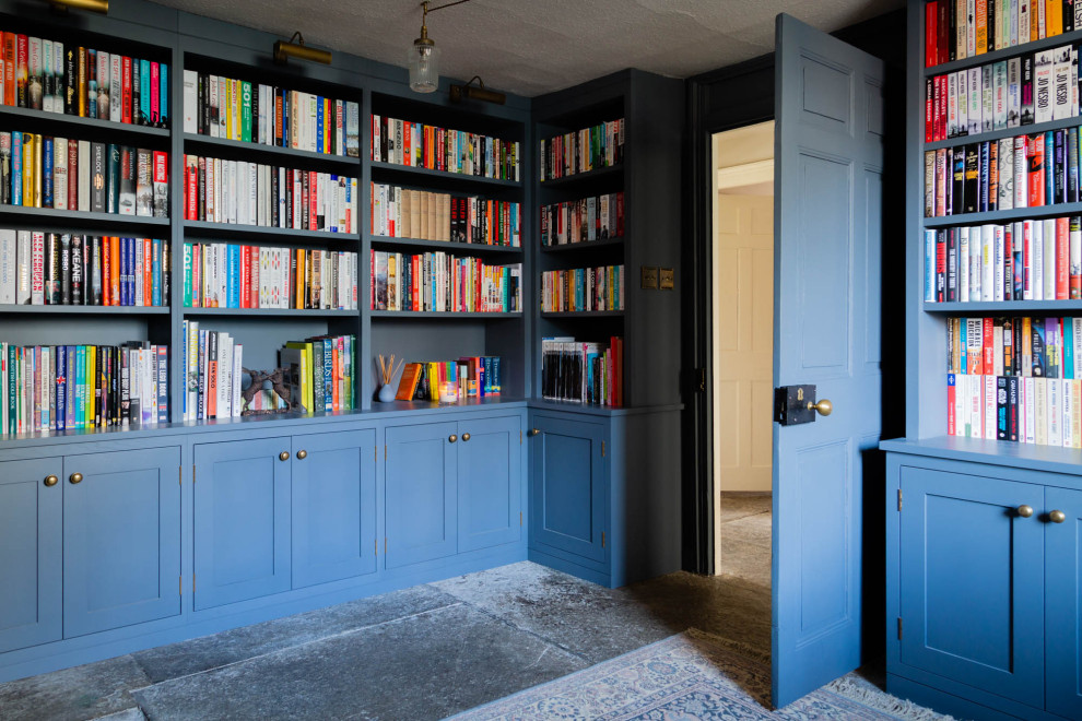 Foto på ett mellanstort vintage vardagsrum, med ett bibliotek, blå väggar, skiffergolv, en öppen vedspis, en spiselkrans i sten och grått golv