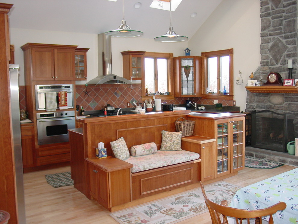 Mountain style l-shaped light wood floor kitchen photo in Boston with an undermount sink, shaker cabinets, medium tone wood cabinets, terra-cotta backsplash, stainless steel appliances and an island