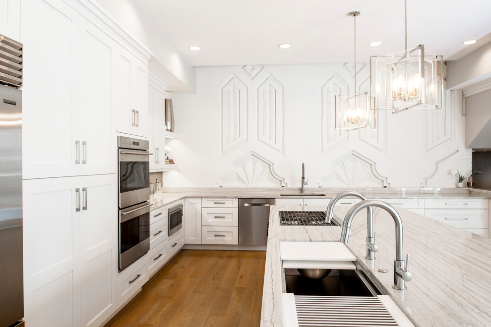 Example of a large transitional medium tone wood floor and brown floor open concept kitchen design with an undermount sink, recessed-panel cabinets, white cabinets, quartzite countertops, brown backsplash, ceramic backsplash, stainless steel appliances, an island and white countertops