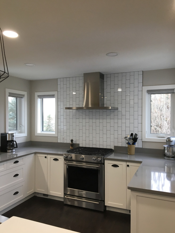 Kitchen - mid-sized transitional u-shaped dark wood floor and brown floor kitchen idea with a farmhouse sink, shaker cabinets, white cabinets, quartzite countertops, white backsplash, subway tile backsplash, stainless steel appliances, an island and gray countertops