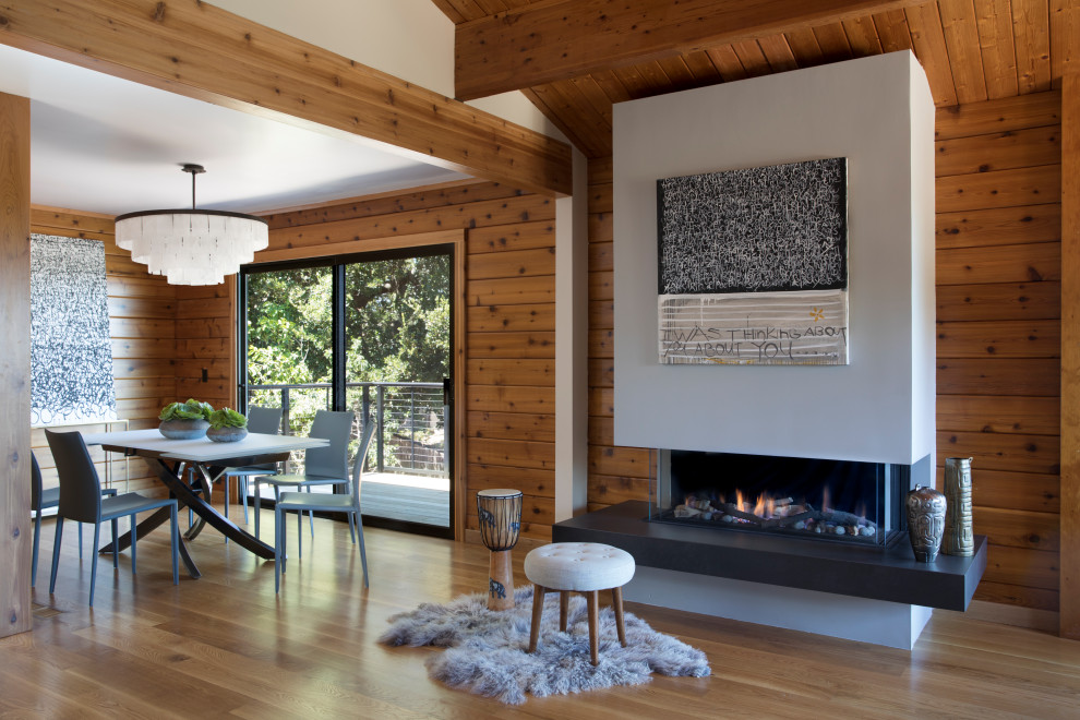 This is an example of a mid-sized contemporary open plan dining in San Francisco with brown walls, medium hardwood floors, a ribbon fireplace, beige floor, a wood fireplace surround, vaulted and wood walls.
