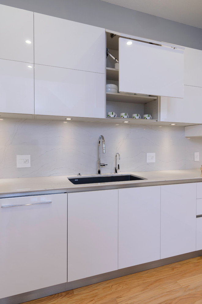 Photo of a mid-sized contemporary galley separate kitchen in Miami with a single-bowl sink, flat-panel cabinets, white cabinets, quartz benchtops, white splashback, panelled appliances, light hardwood floors and with island.